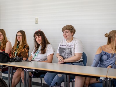 Junge Menschen sitzen in einer Reihe an einem Tisch und nehmen an einem Workshop teil.