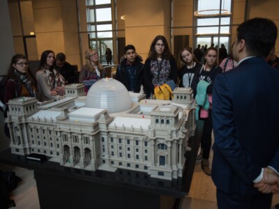 Eine Gruppe junger Menschen und ein Mann vom Besucherdienst stehen um ein Modell des Reichstagsgebäudes herum.