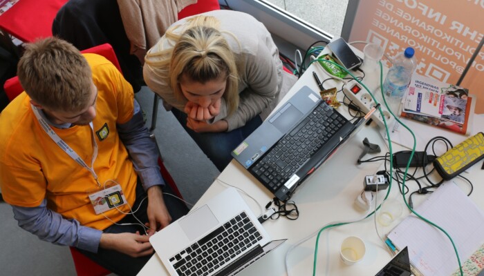 Zwei junge Menschen sitzen vor einem Laptop und schauen darauf etwas an.